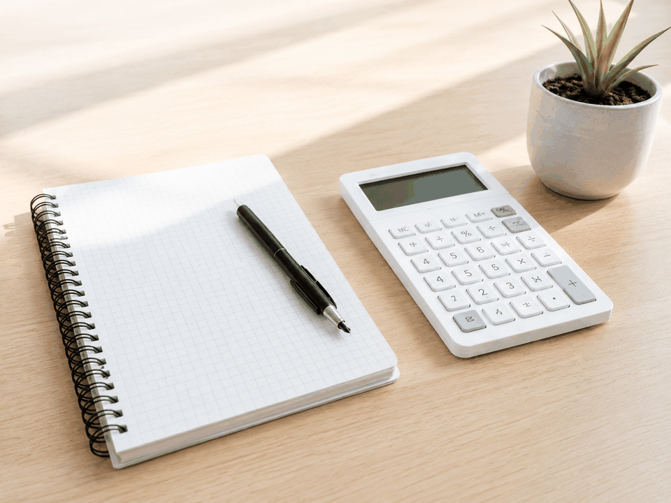 A clean budgeting desk scene with a calculator, notebook, pen, and small plant